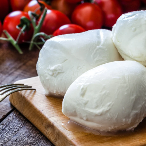 Balls of fresh homemade mozzarella on a wooden cutting board, surrounded by vine-ripened cherry tomatoes and a bottle of olive oil, set on a rustic wooden table.