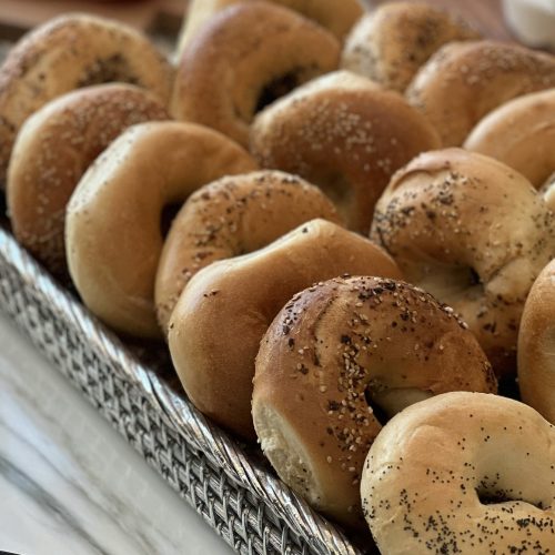 Homemade New York style bagels with sesame, poppy seed, and everything toppings arranged on a serving tray on a kitchen counter.