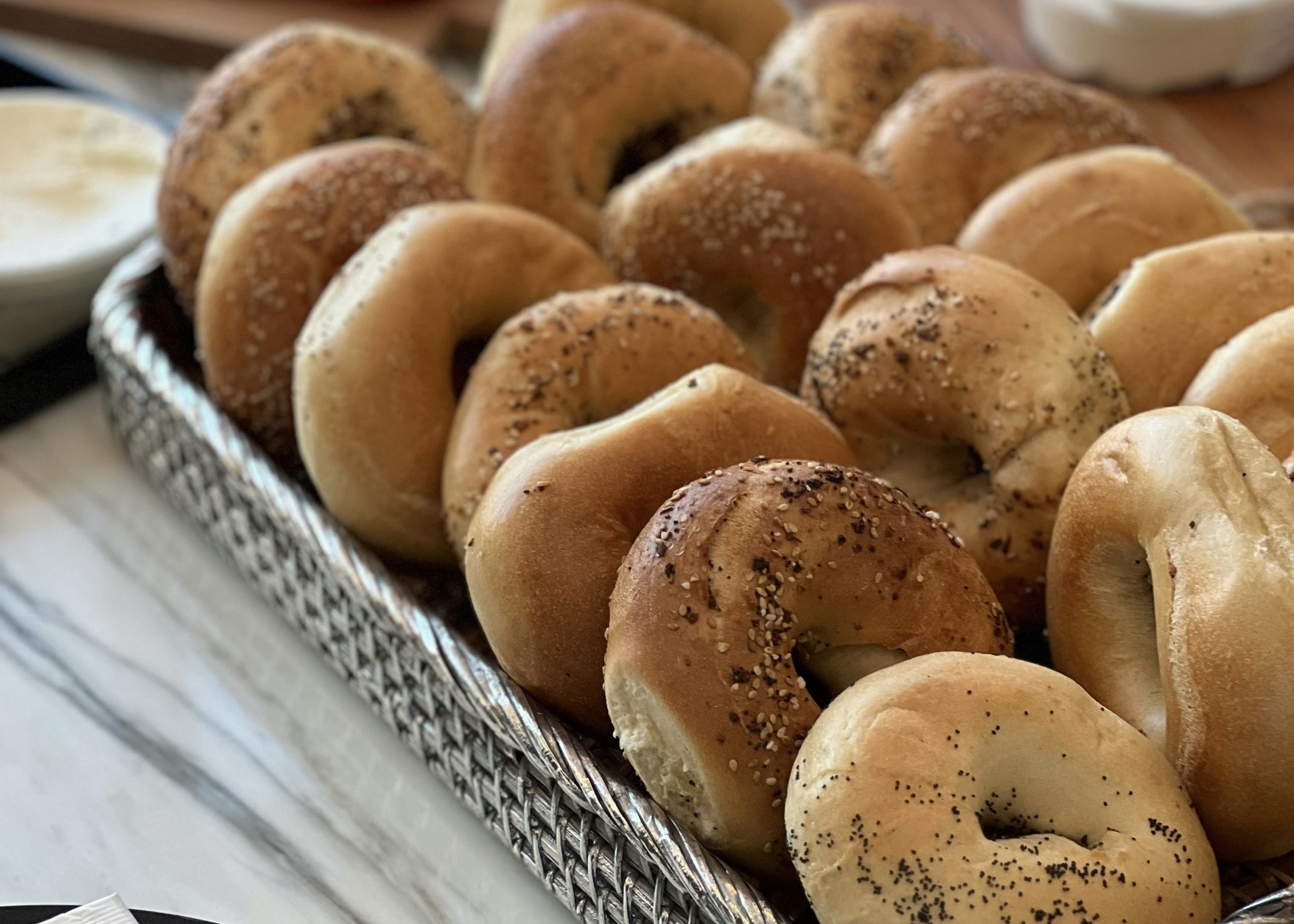 Homemade New York style bagels with sesame, poppy seed, and everything toppings arranged on a serving tray on a kitchen counter.